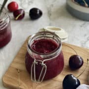 fresh homemade cherry jam, served in a jar, with cherries in the background.