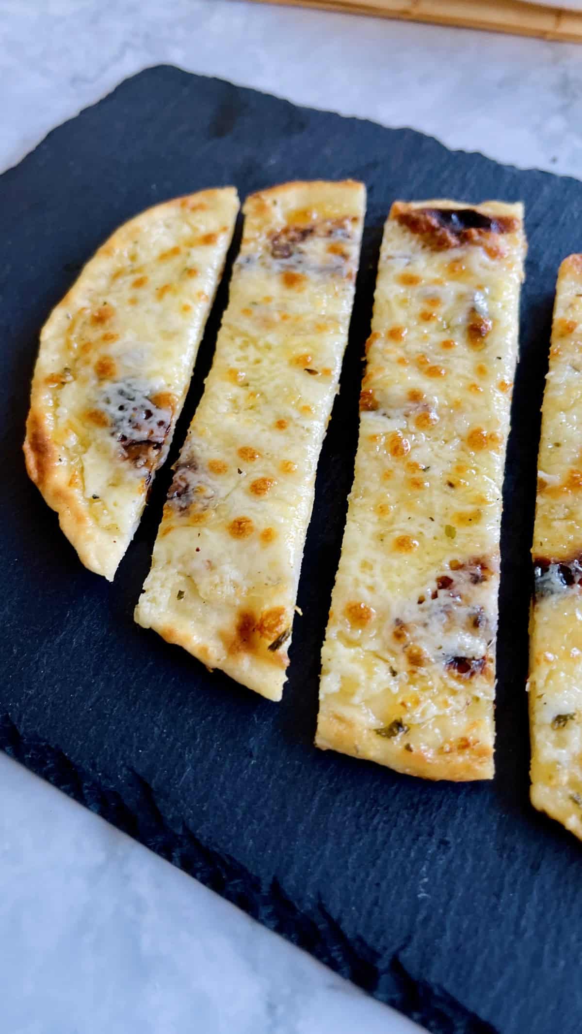 golden cheesy garlic naan bread slices served on a black plate.