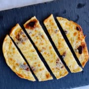 freshly made golden cheesy garlic naan bread slices served on a black plate.