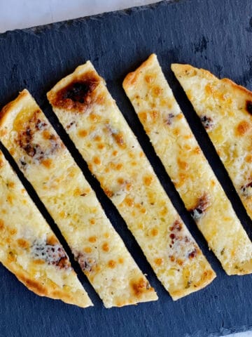 freshly made golden cheesy garlic naan bread slices served on a black plate.