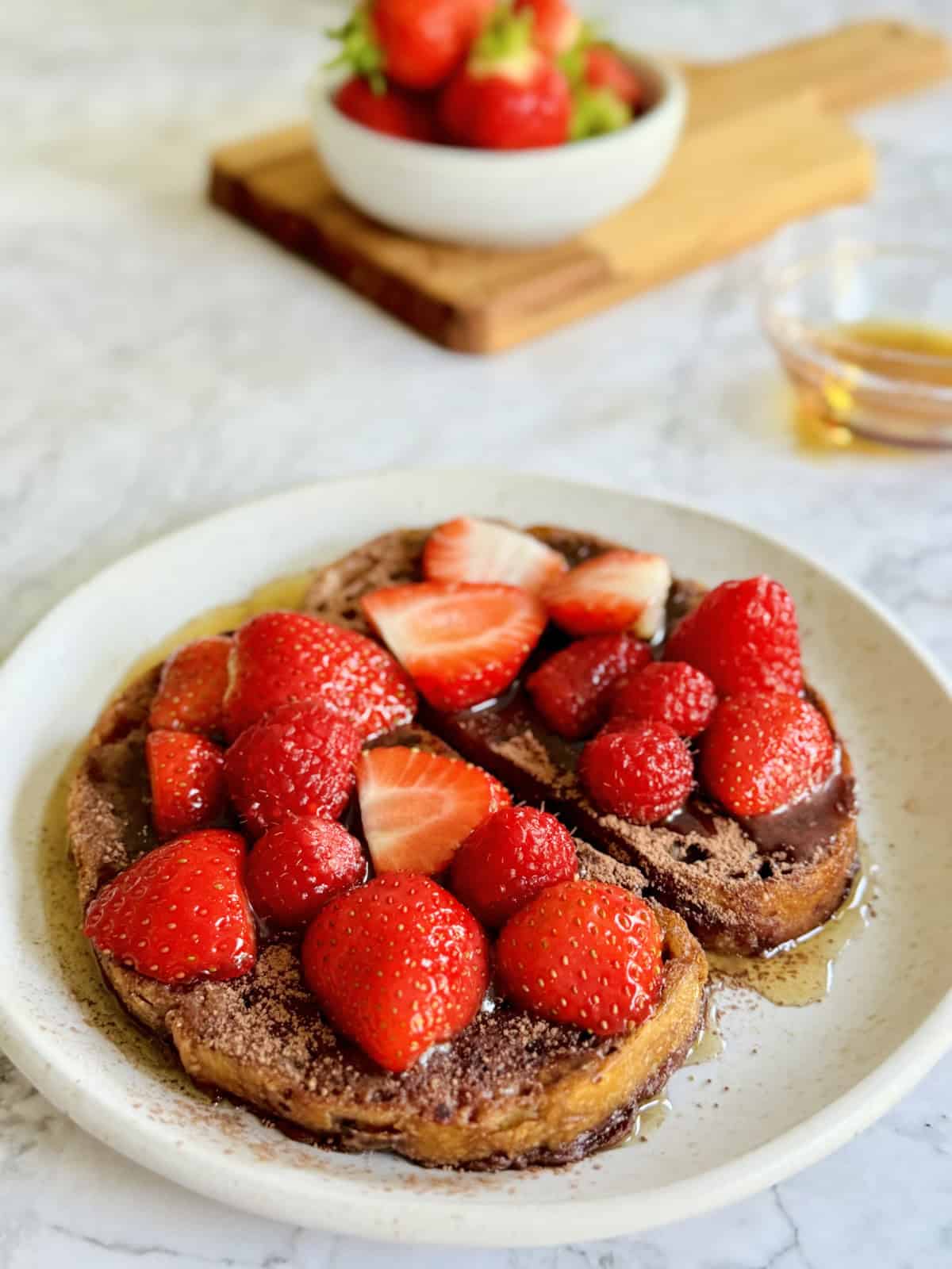 Fresh homemade chocolate French toast, with warm maple syrup, a sprinke of cacao powder and and fresh berries.