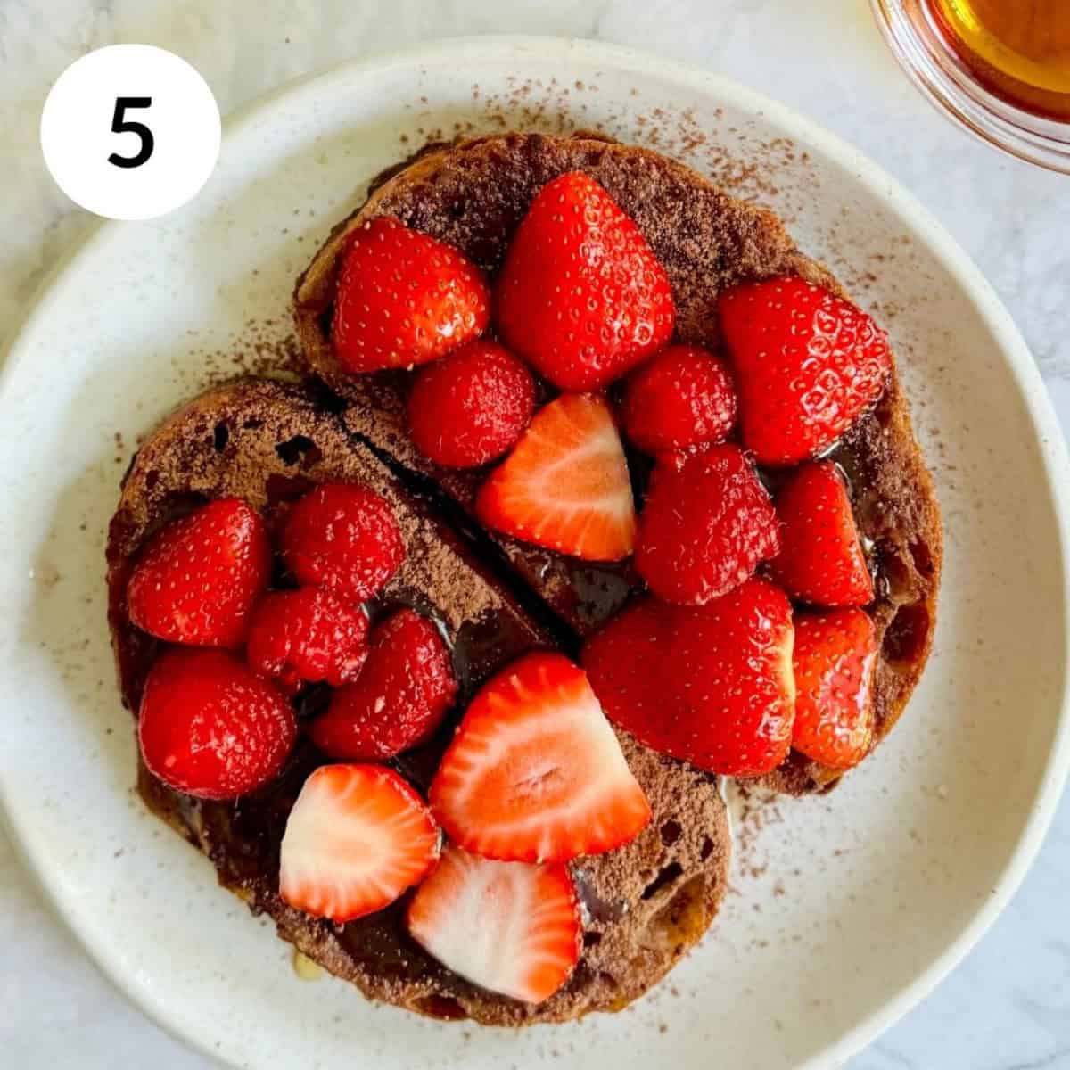 topping chocolate French toast slices with maple syrup, berries and a sprinkle of cacao powder.