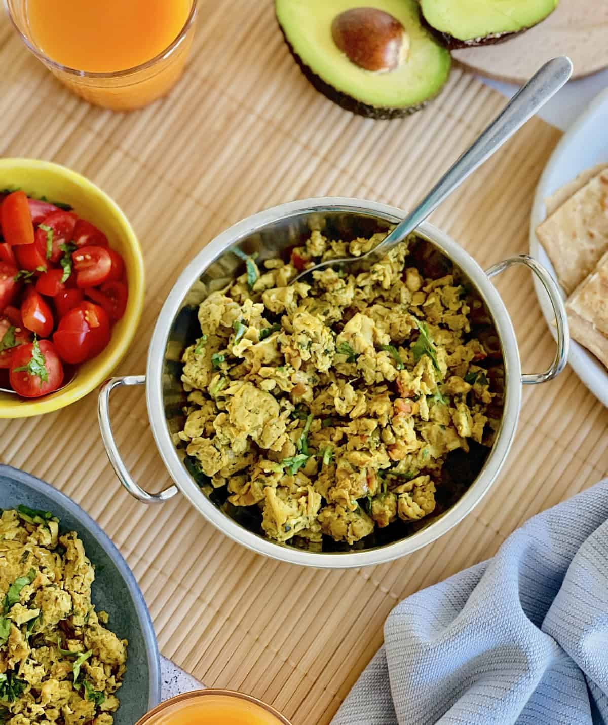 fresh masala scrambled eggs served in dish, with salsa and avocado, juice and Indian flatbread in the background.