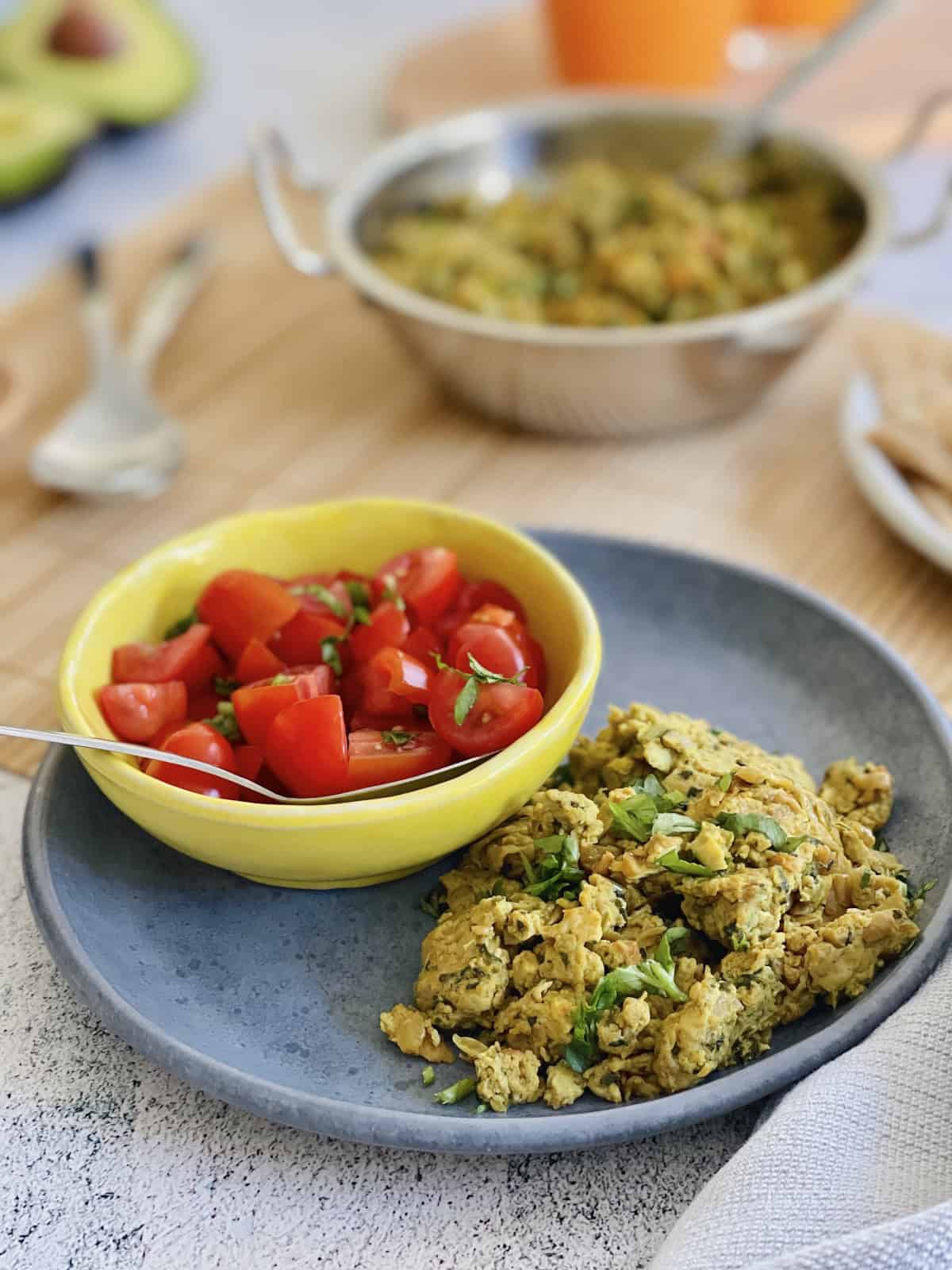 Indian masala scrambled eggs served in blue plate with fresh salsa in a yellow bowl.