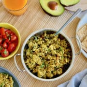 fresh Indian-style masala scrambled eggs served in dish, with tomato salsa and avocado and orange juice.