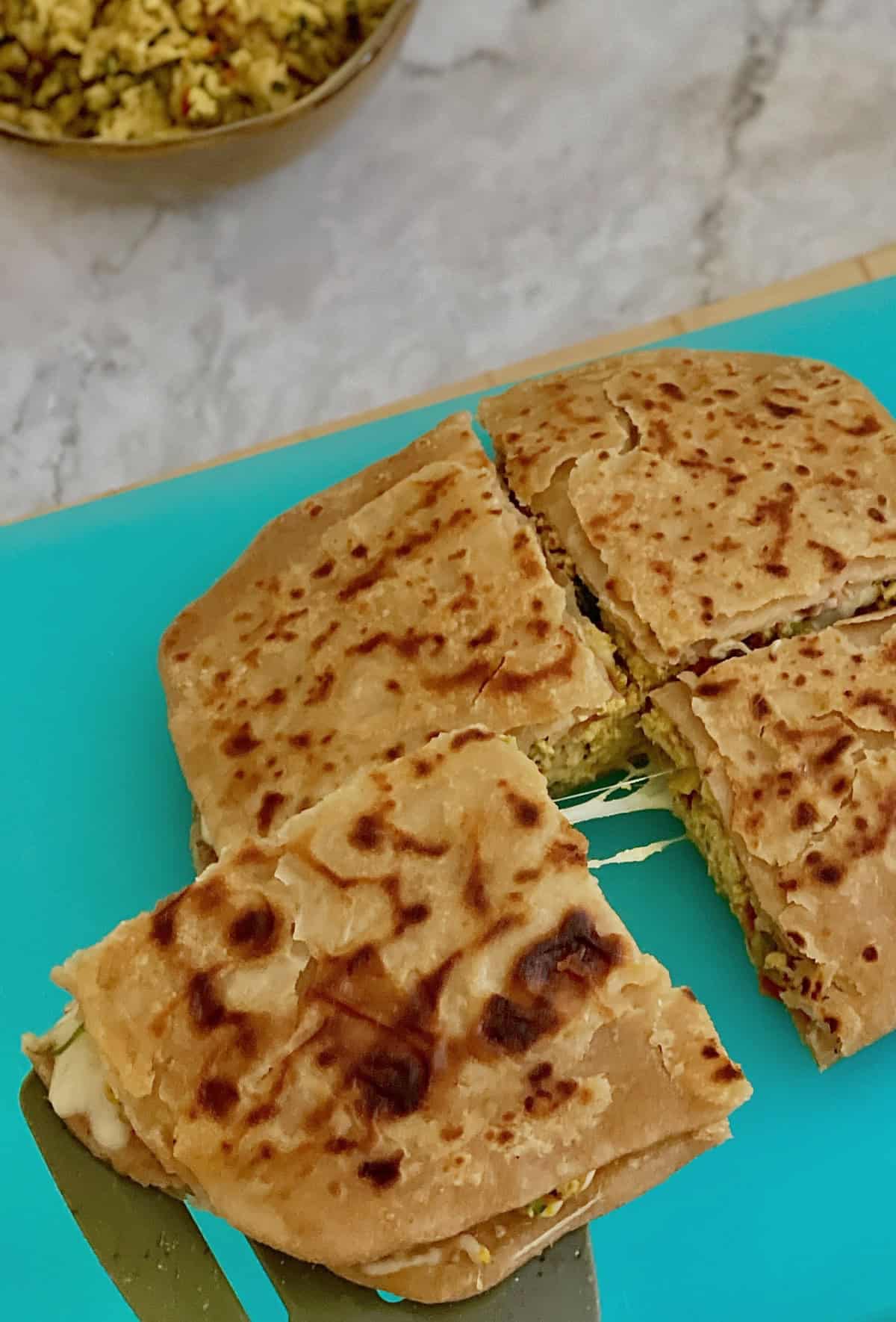 lifting the cheesy masala egg paratha quarter with a spatula.