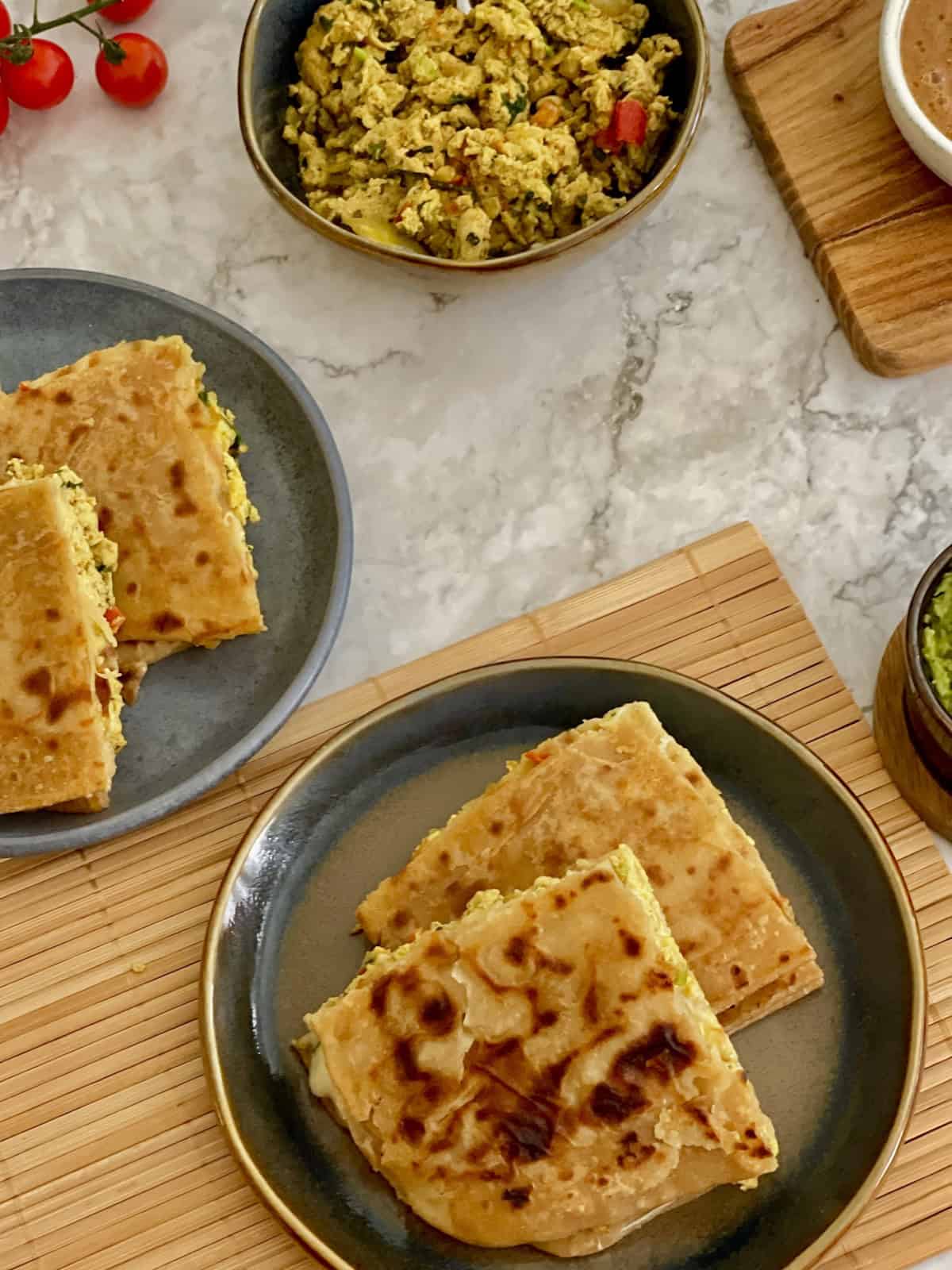 crispy masala egg paratha quarters on a plate, with guacamole and salsa.