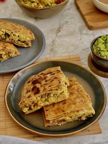 crispy masala egg paratha quarters on a plate, with fresh guacamole and salsa.