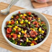 black bean corn salsa in a bowl, plum tomatoes in background.
