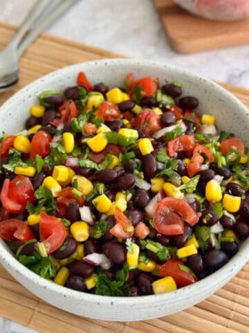 black bean corn salsa in a bowl, plum tomatoes in background.