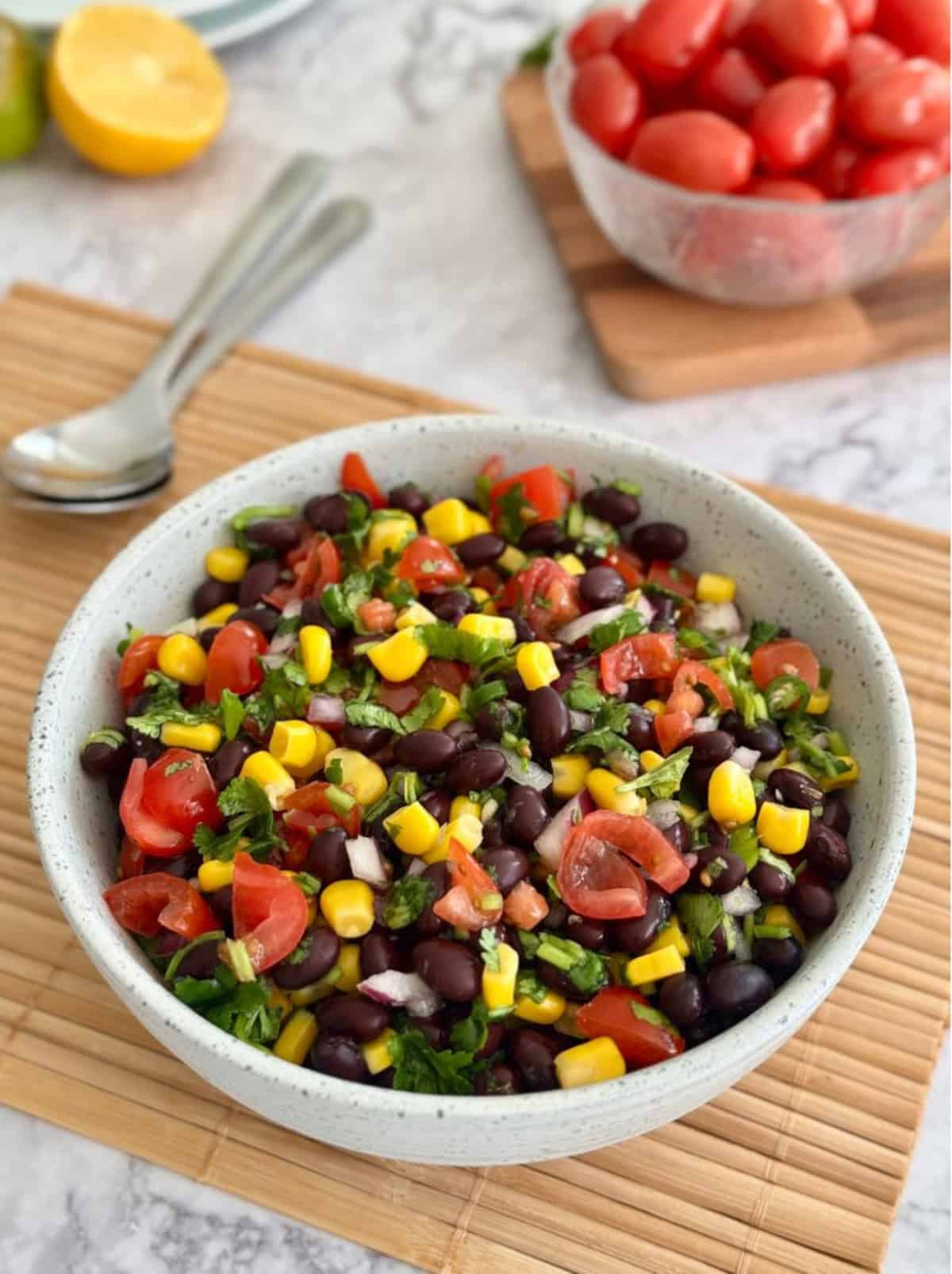 black bean corn salsa in a bowl, plum tomatoes, lemon and lime in background.