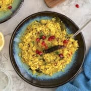 fresh lemon rice, in a blue plate, topped with pomegranate.