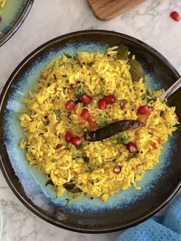 fresh lemon rice, in a blue plate, topped with pomegranate.