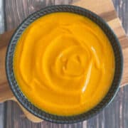 A bowl of sweet potato and red pepper soup on a cutting board.