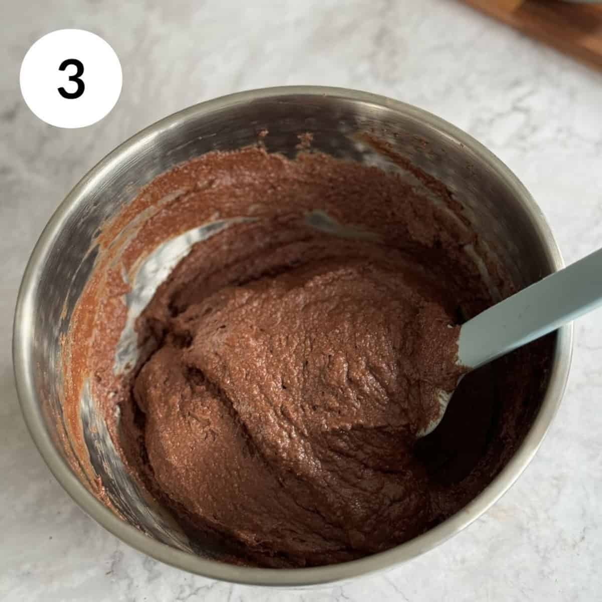 adding dry ingredients to the wet ingredients to form a pumpkin chocolate brownie batter.