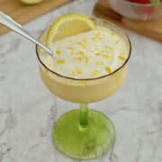 lemon cottage cheese pudding served in a glass, topped with fresh lemon zest, with strawberries in a bowl on the side.