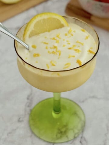 lemon cottage cheese pudding served in a glass, topped with fresh lemon zest, with strawberries in a bowl on the side.