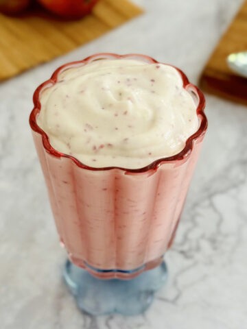nectarine cottage cheese pudding in pink serving glass, with spoon, nectarine and cutting board in background.