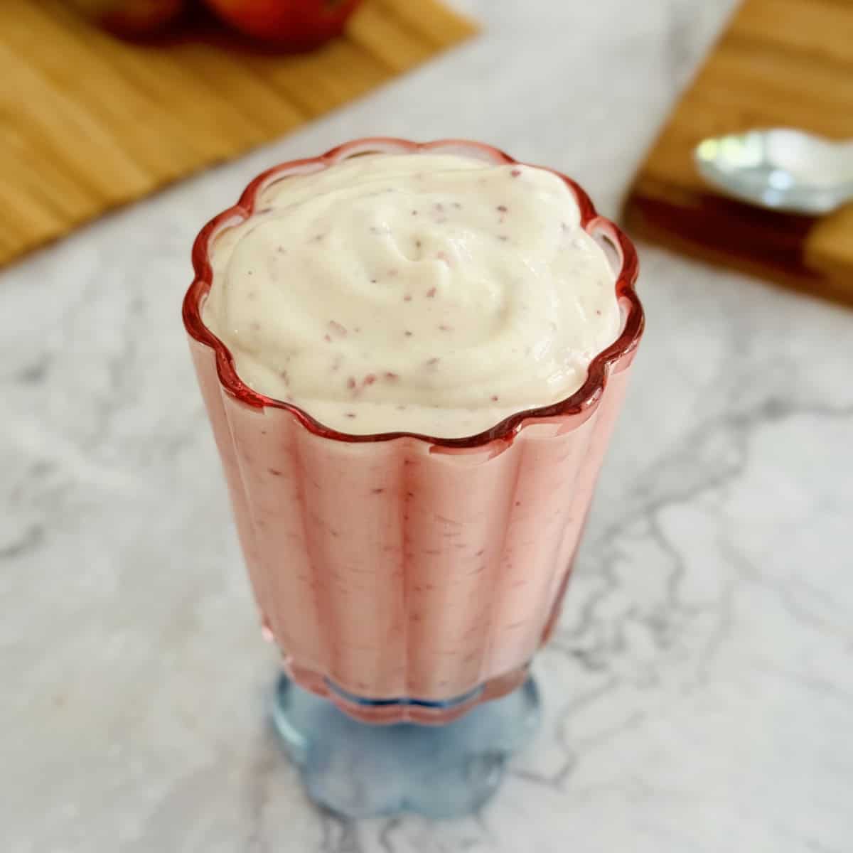 nectarine cottage cheese pudding in pink serving glass, with spoon, nectarine and cutting board in background.
