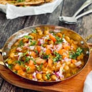chana masala in a serving dish, garnished with fresh coriander, tomatoes, onions.