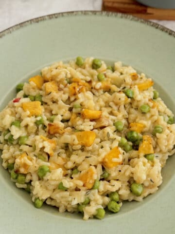 roasted pumpkin and pea risotto served in wide blue plate.