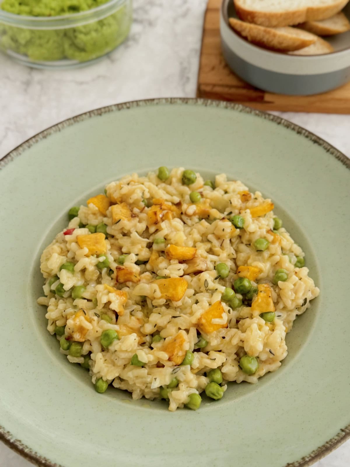 roasted pumpkin and pea risotto served in blue plate, with bread and avocado mash in background.