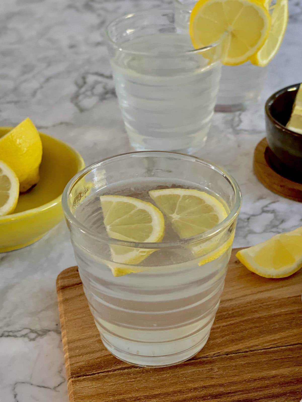 lemon water, with sliced lemon wedges, lemons in background.