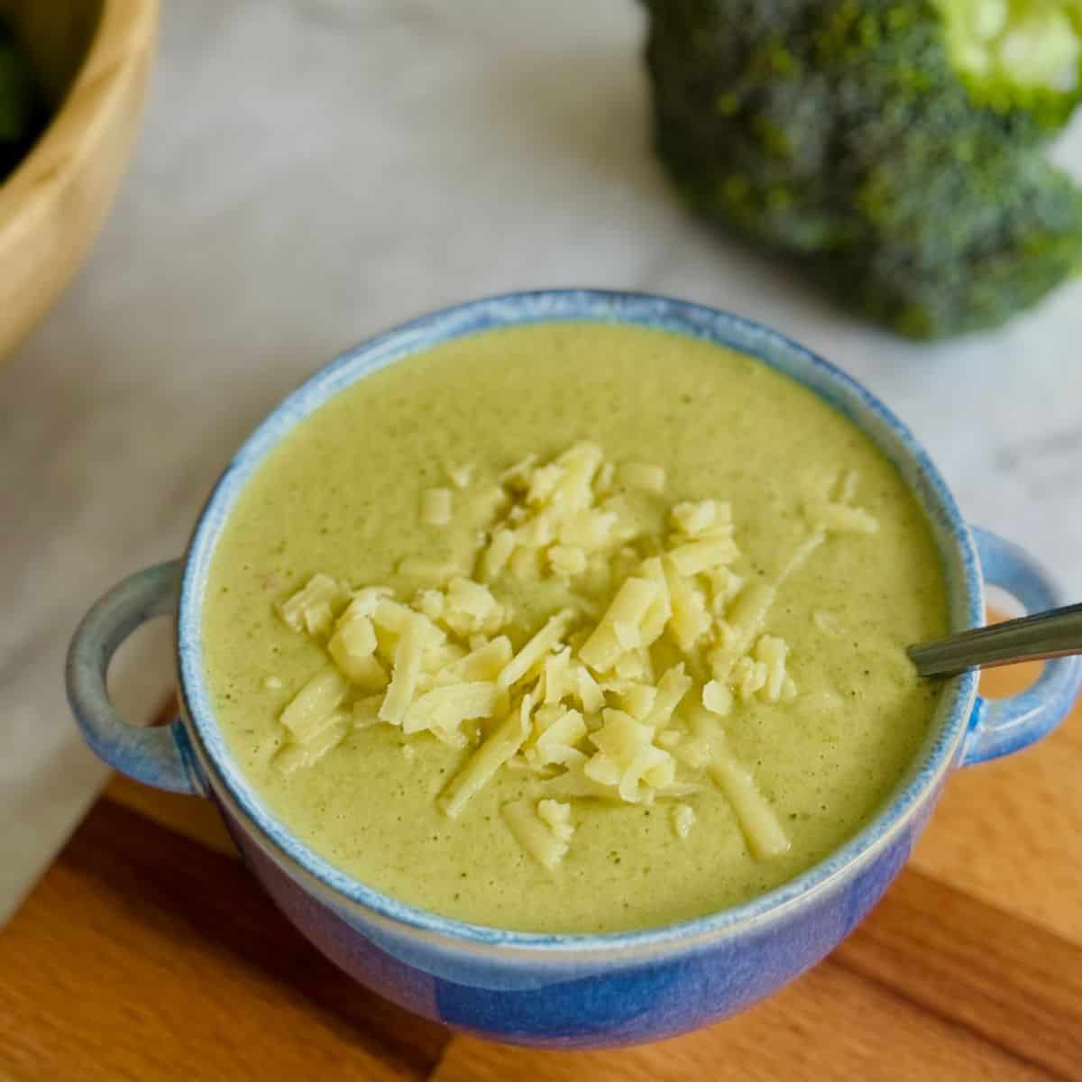 broccoli and cheddar soup in blue bowl, topped with cheese, salad in background.