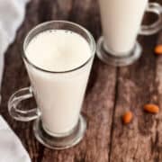 fresh homemade almond milk served in glasses, with almonds in the background.