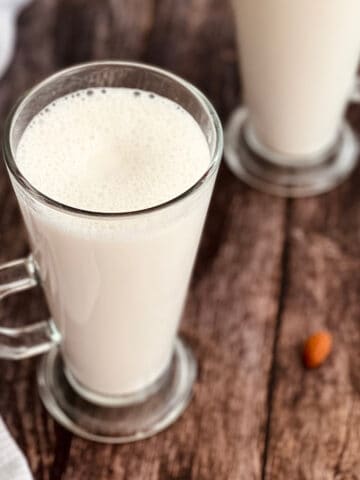 fresh homemade almond milk served in glasses, with almonds in the background.