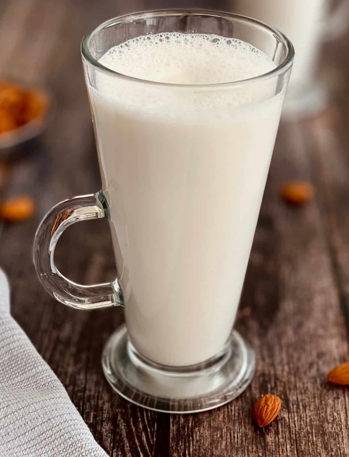 homemade almond milk served in a glass, with almonds on the side.